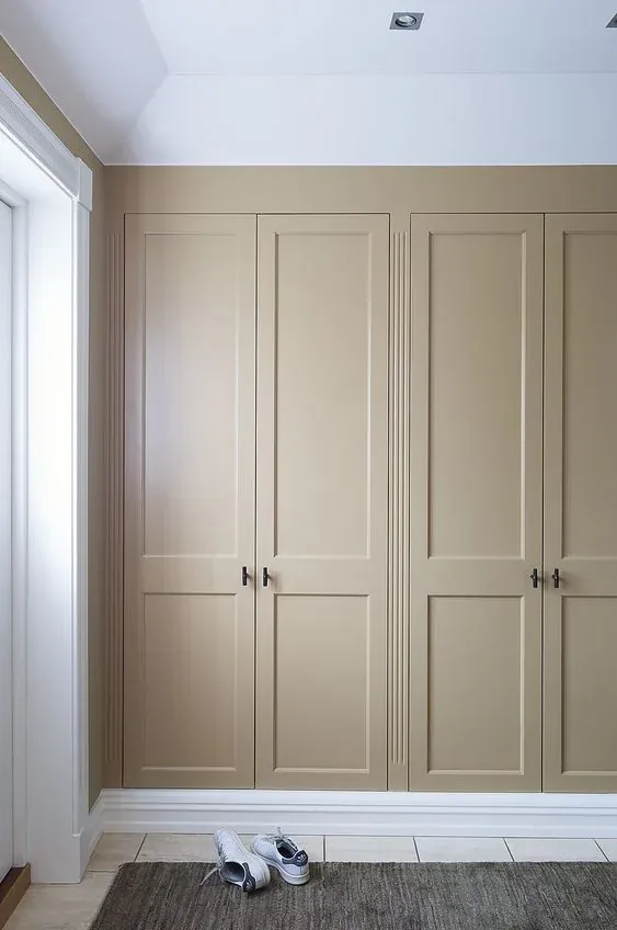 Kamerhoge inbouwkast met beige paneeldeuren over de volle wandbreedte in een hal