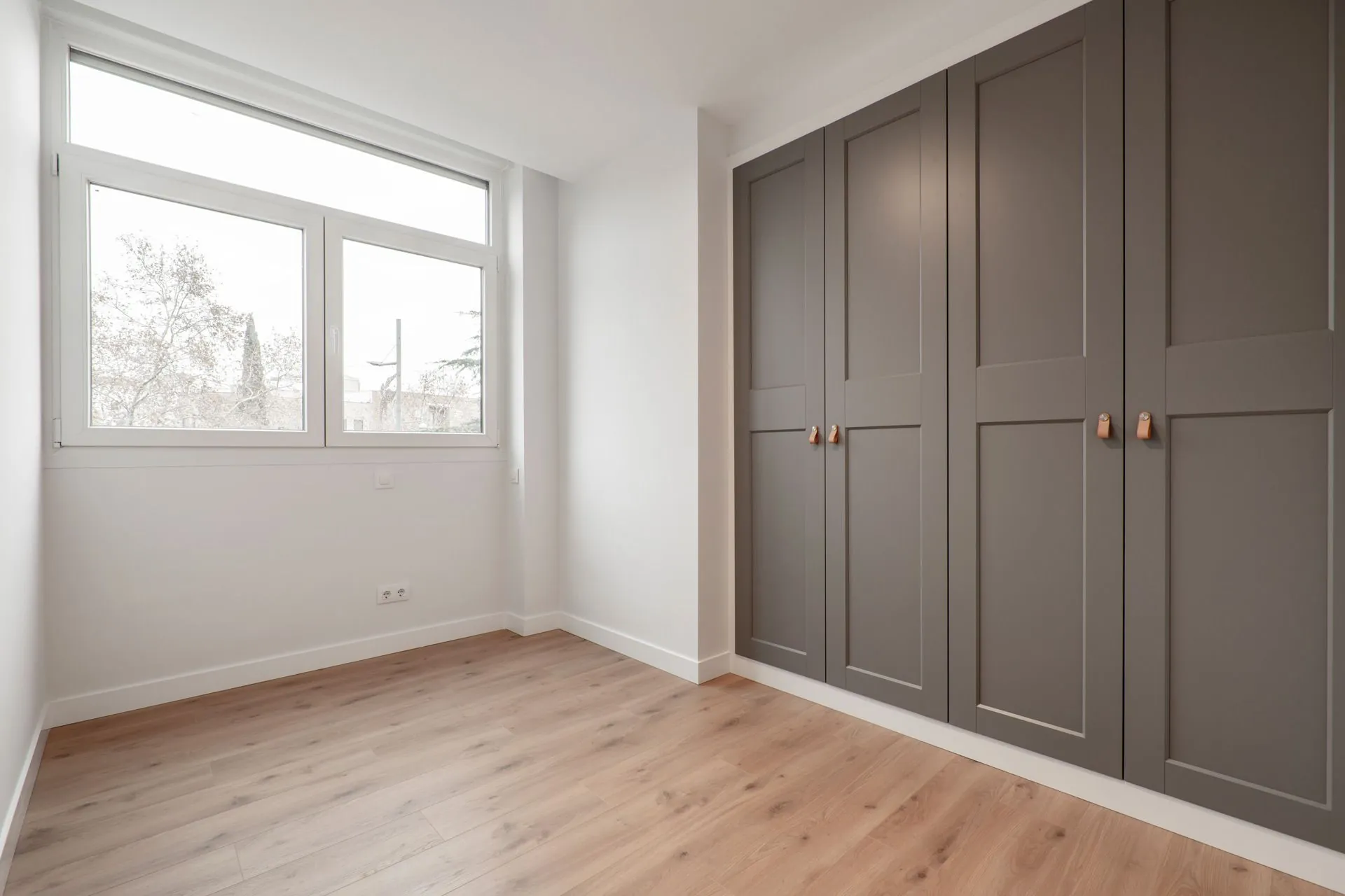 Lichte slaapkamer met een kamerhoge inbouwkast met taupe paneeldeuren en een eiken vloer