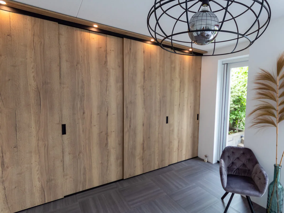 Wandbrede kastenwand in eikendecor met een verlichte bovenlijst en zwarte grepen
