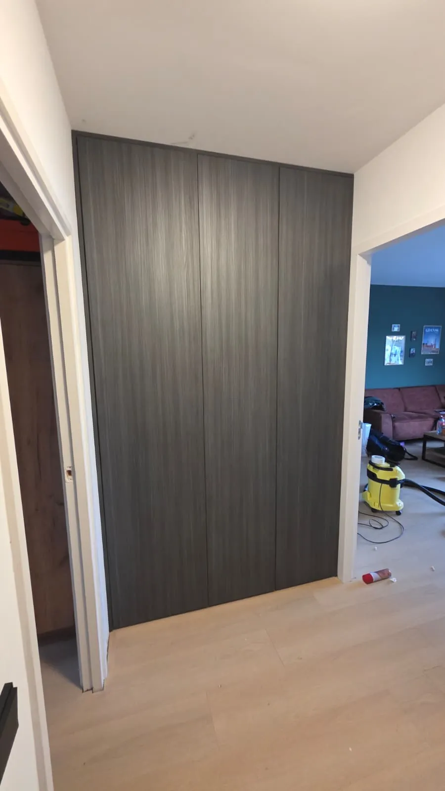 Gesloten kastenwand in houtdecor tussen hal en woonkamer, waarachter de meterkast is weggewerkt