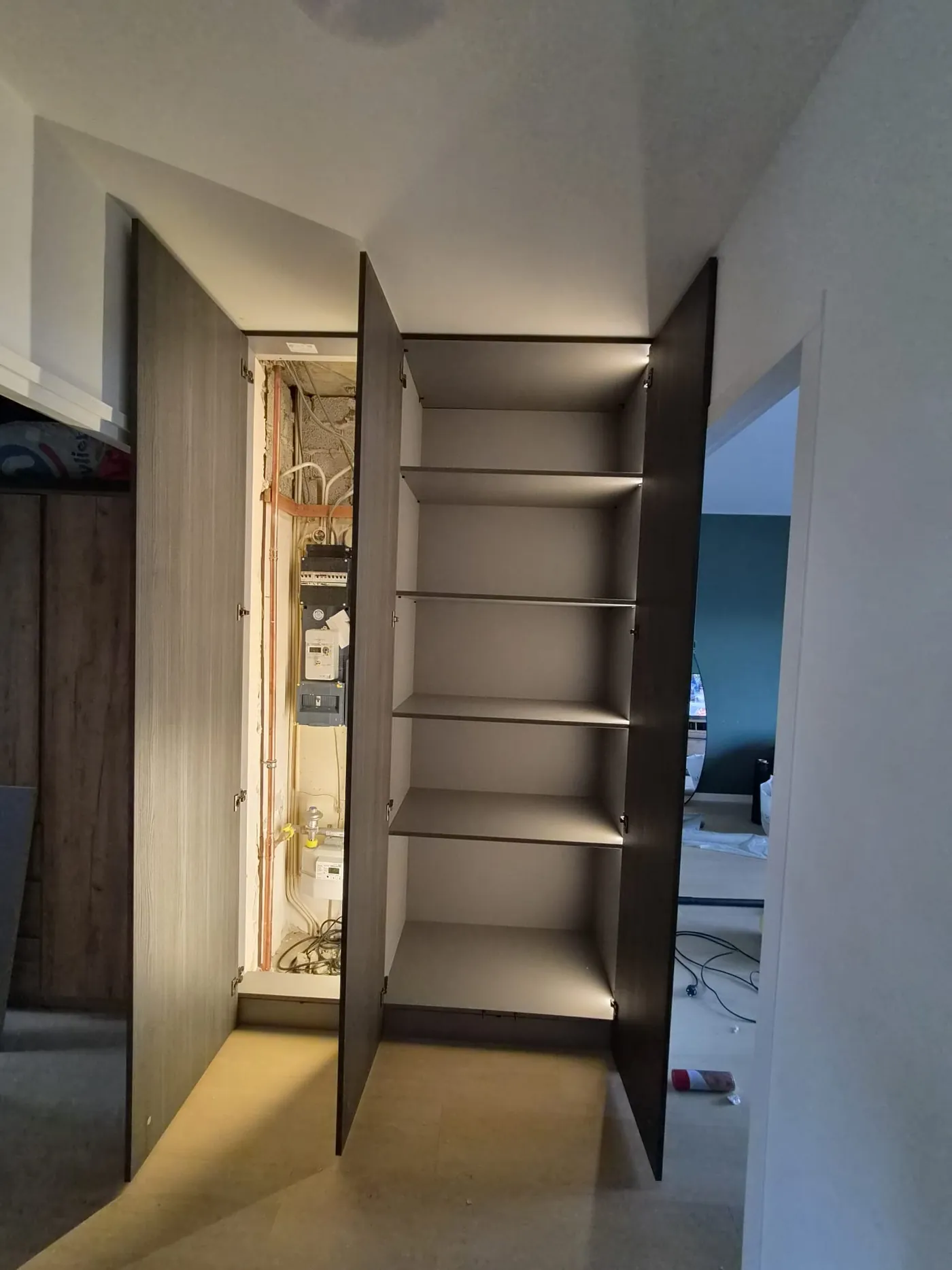 Geopende maatwerk kastenwand met ingebouwde meterkast en cv-installatie links en verlichte legplanken rechts